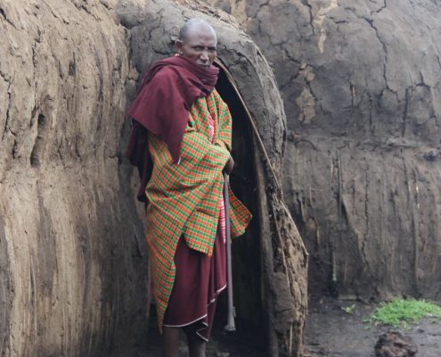 Durante su safari de 7 días por Tanzania tendrá la oportunidad de conocer a la gente y la cultura locales, como este anciano masai frente a un boma tradicional de adobe.
